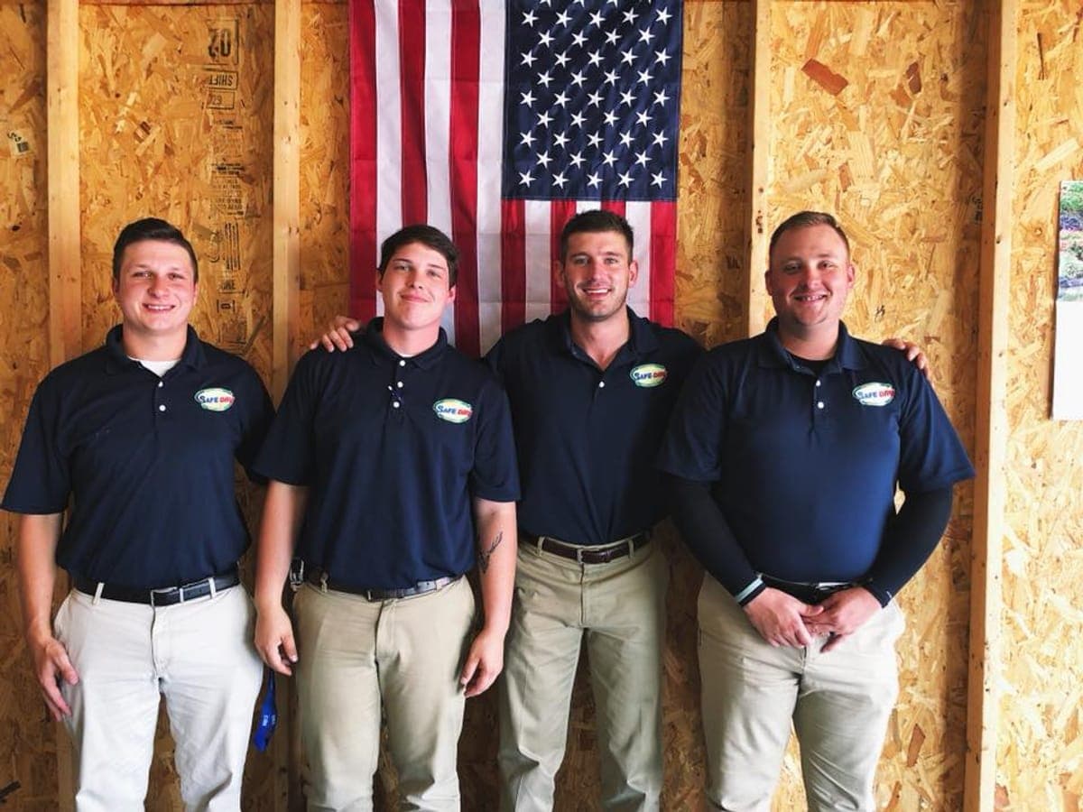 Four Safe-Dry team members in branded polos standing in front of an American flag