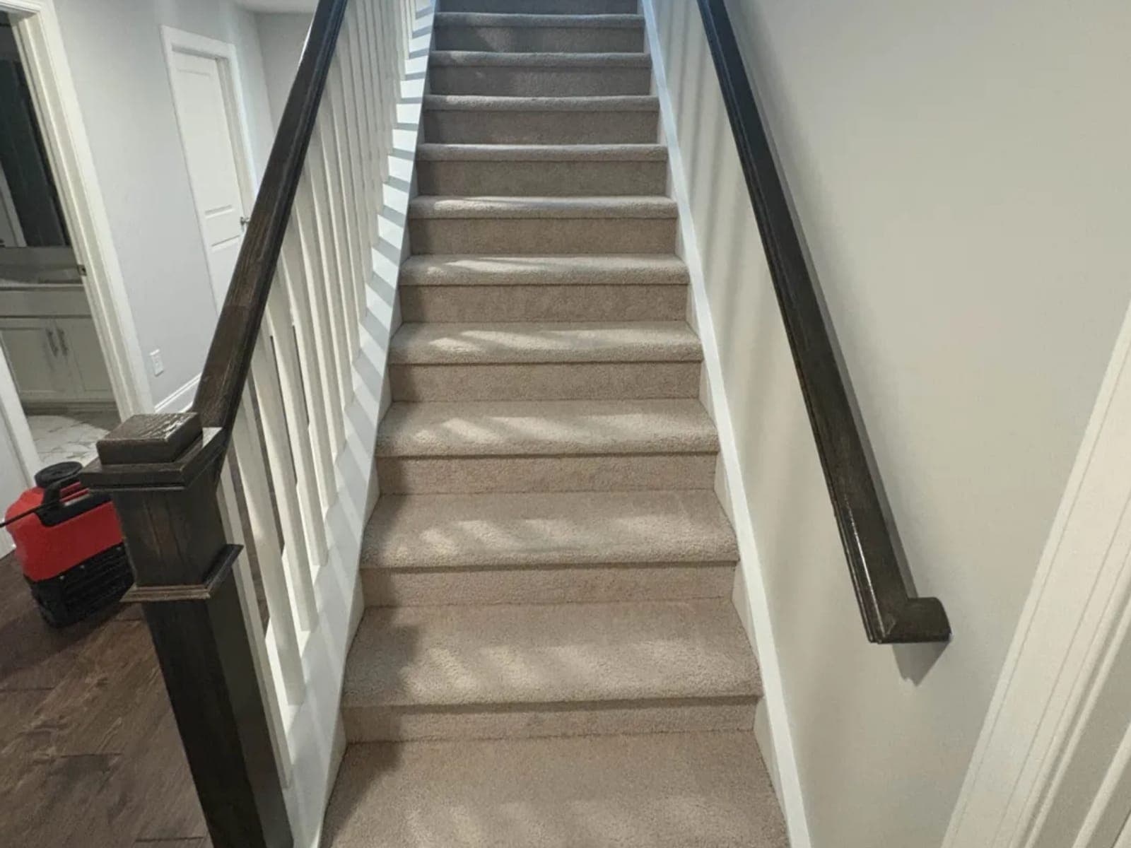 Red air mover drying the floor at the base of a carpeted staircase